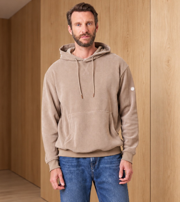 Homme portant un pull côtelé beige à capuche devant un fond en bois clair